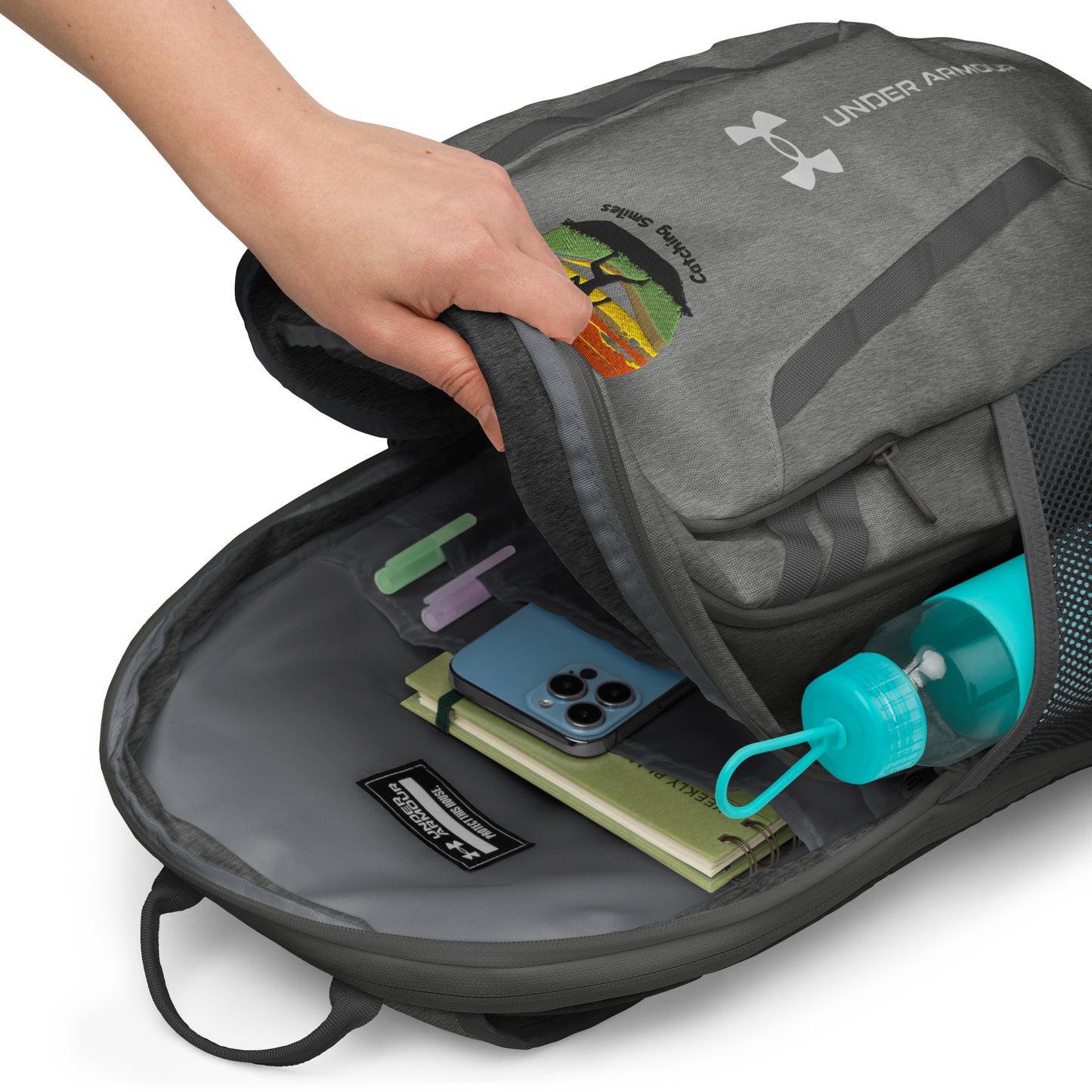 Gray Under Armour backpack with items like a phone and water bottle inside, on a white background