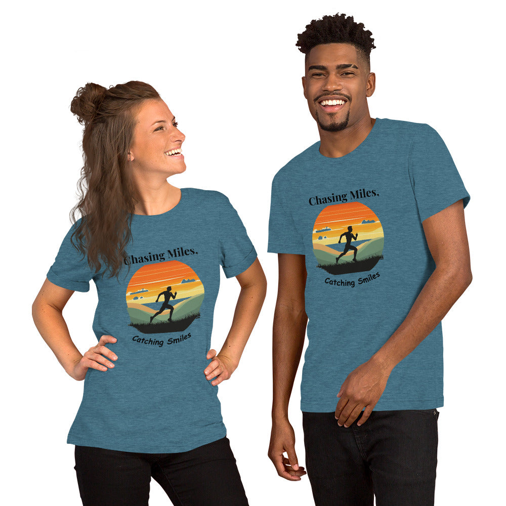 A man and a woman standing and smiling, wearing green crew neck t-shirts with a graphic text 'Chasing Miles, Catching Smiles' on the front.