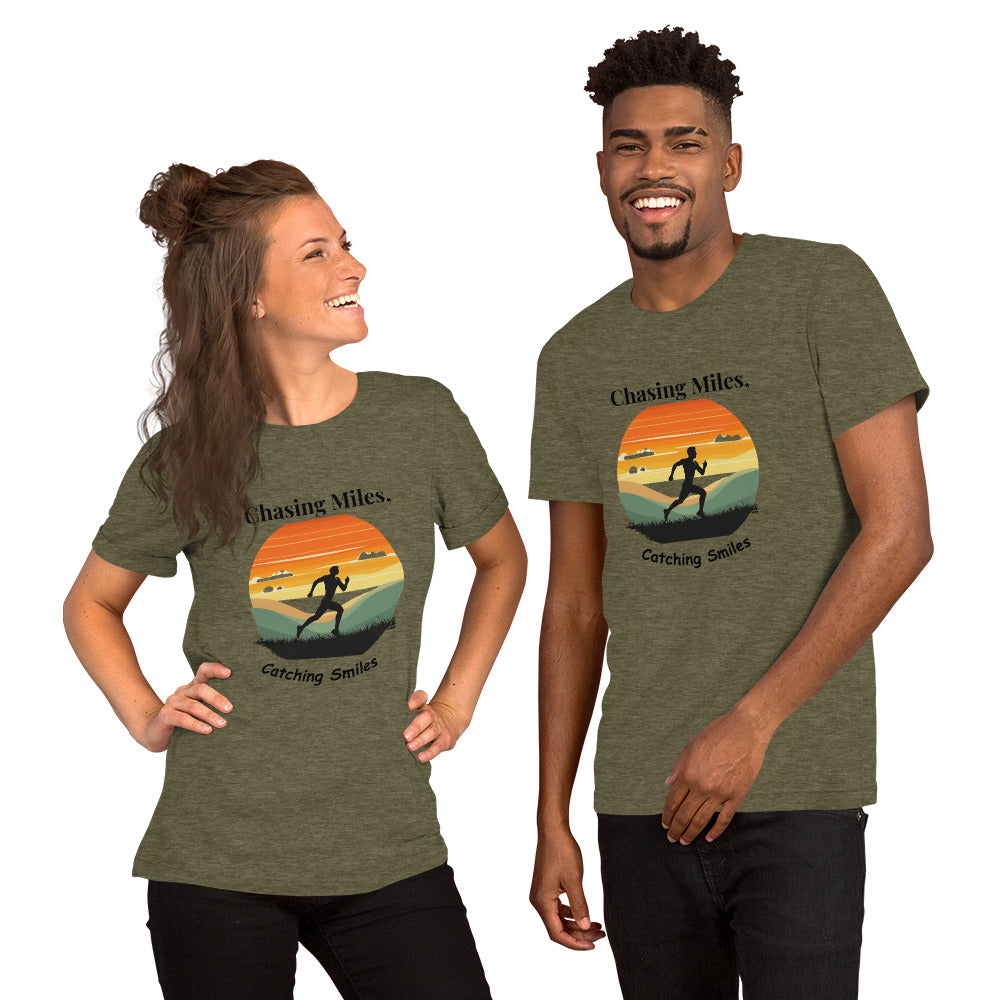 A man and a woman standing and smiling, wearing green crew neck t-shirts with a graphic text 'Chasing Miles, Catching Sunsets' on the front.